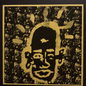 A square black and gold art print featuring a stylized face with radiating gold shapes on a textured black background, bordered by a gold frame against a dark backdrop.