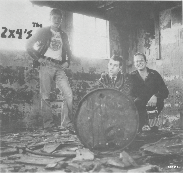 Three people posing with a barrel in a dilapidated building, with 'The 2x4's' text.